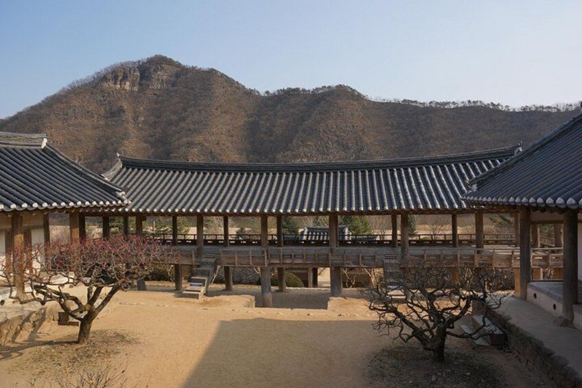 A traditional Korean pavilion with tiled roofs, surrounded by a courtyard with benches and a tree. 5