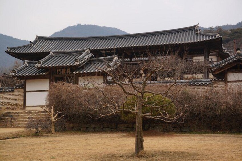 A traditional Korean building with a tiled roof, surrounded by a dry field and bare trees. 1