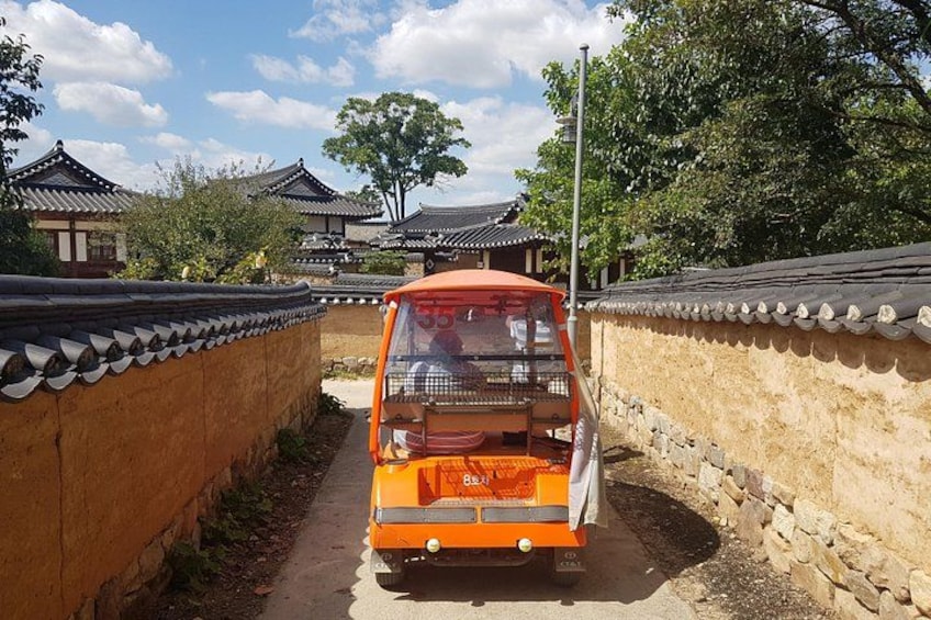 A traditional Korean building with a narrow alleyway and an orange vehicle parked in front. 2