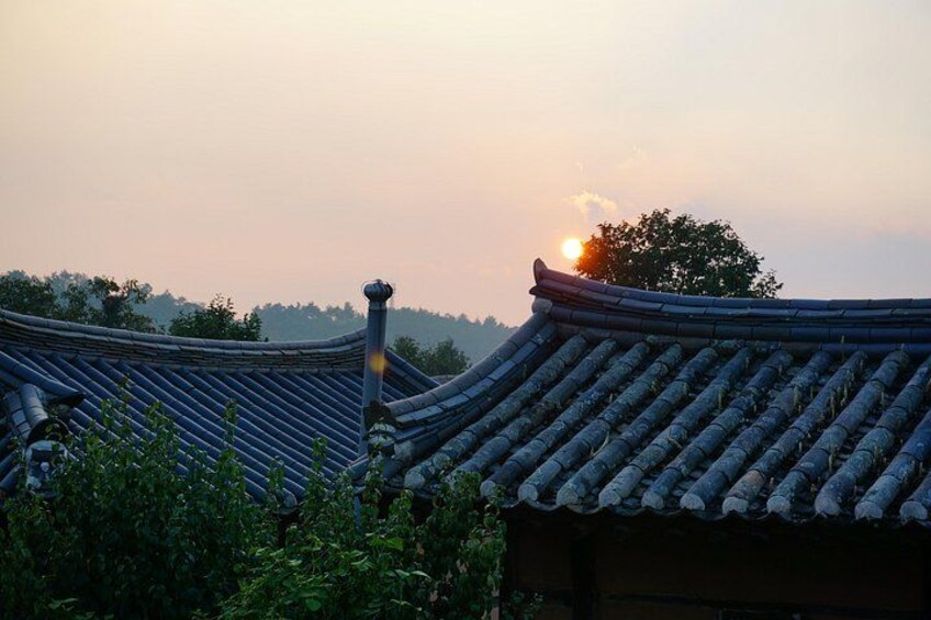 Traditional Korean rooftops, a setting sun, and a tree in the background. 2
