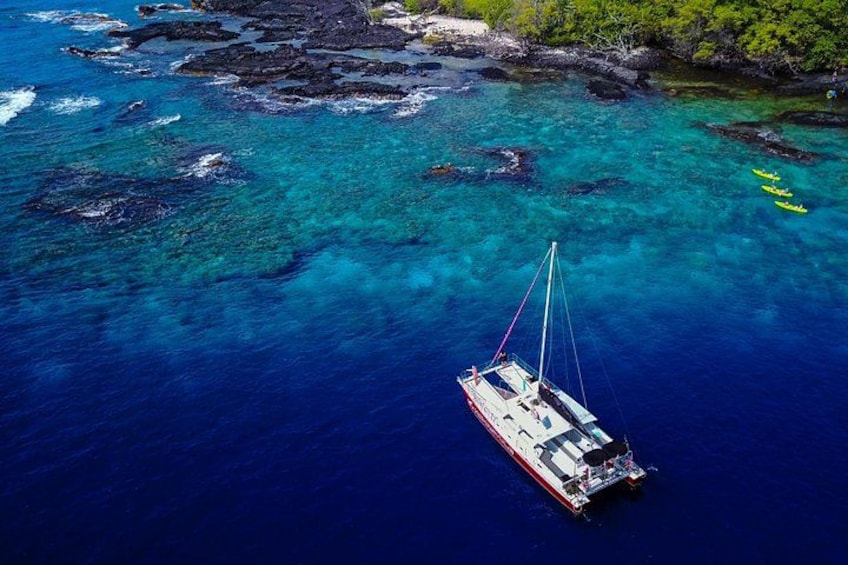 A sailboat on clear turquoise waters with rocky outcrops and greenery in the background. 4