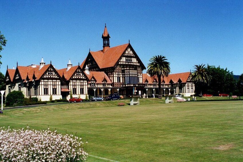 A large, historic building with a prominent tower, surrounded by a well-maintained lawn and palm trees. 3