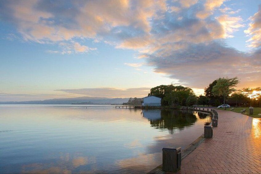A calm lake with a wooden walkway, trees, and a distant building. 4