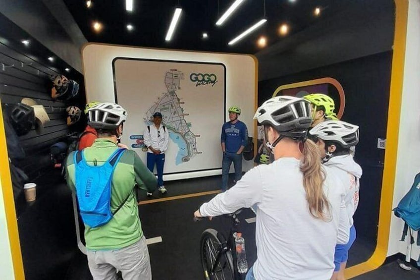 A group of people wearing helmets and cycling gear, gathered around a map on a wall. 5