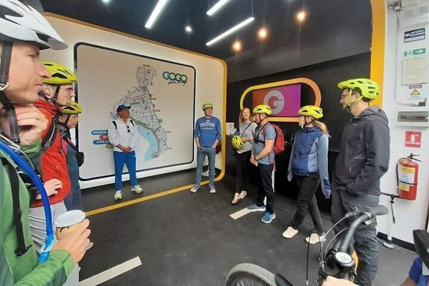 A group of people in helmets and casual clothing standing in a room with a large map on the wall. 4