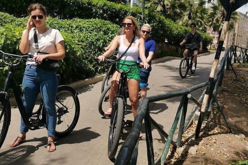 Personas montando bicicletas en un camino pavimentado, flanqueado por follaje. 2