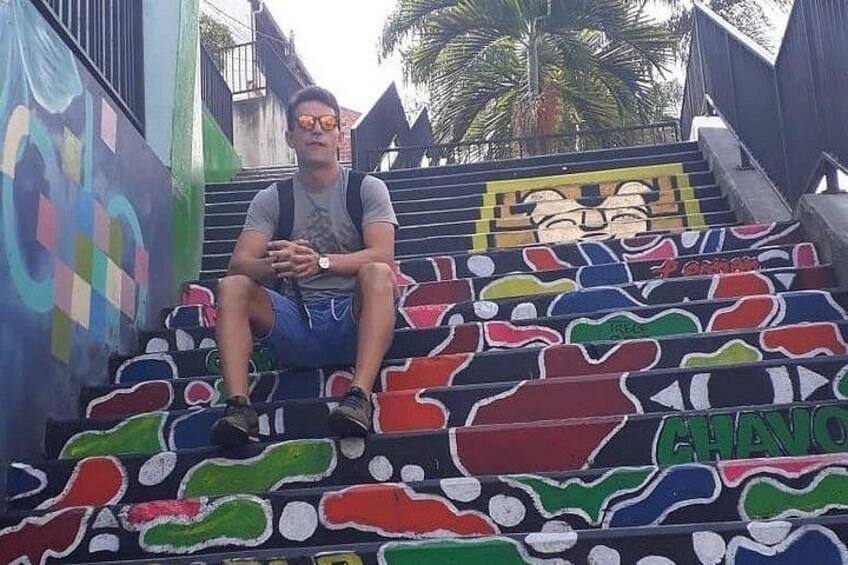 A person sitting on colorful, graffiti-covered stairs with palm trees in the background. 4