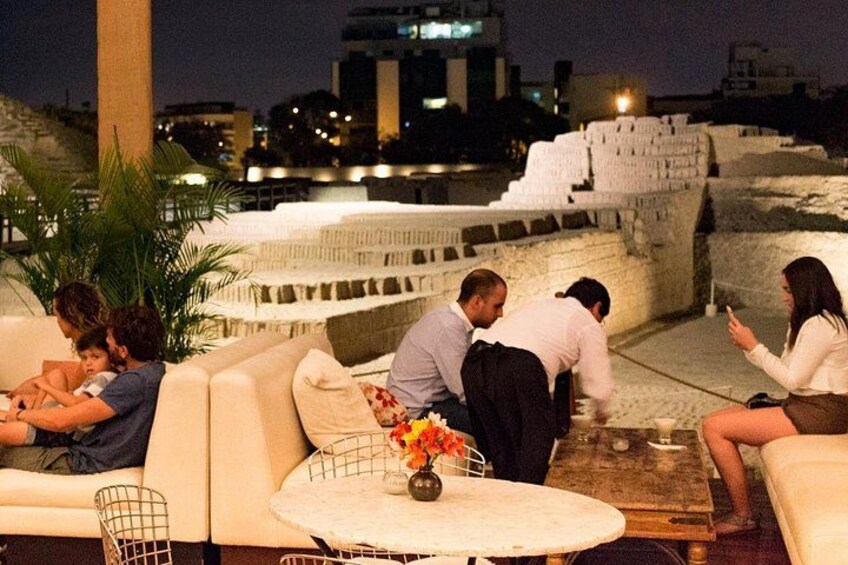 Un bar situé sur un toit, avec des tables à l’extérieur, une table blanche ornée d’un vase de fleurs et, en arrière-plan, une vue sur la ville. 3