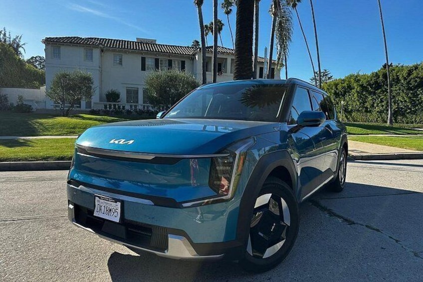 Un Kia SUV azul estacionado en una calle con una casa y palmeras al fondo. 2