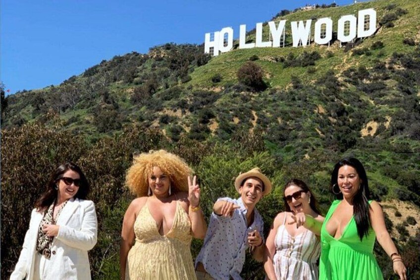 Un gruppo di persone in piedi di fronte al cartello di Hollywood, con un paesaggio collinare sullo sfondo. 4