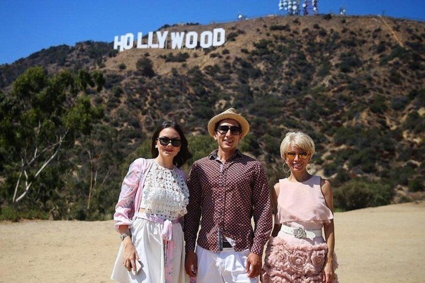 Tre persone in piedi di fronte al cartello di Hollywood, con un paesaggio desertico sullo sfondo. 3