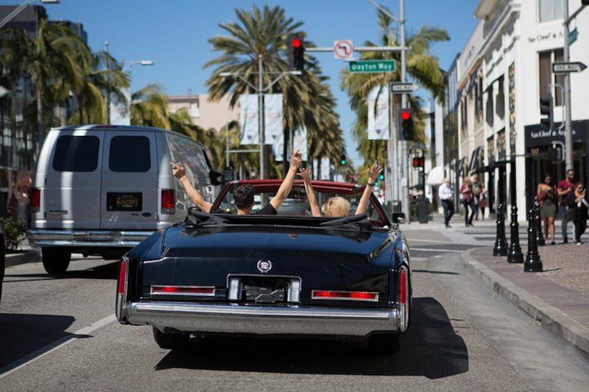 A black convertible with a woman in the passenger seat, a silver van, palm trees, and a street sign for Dayton Road. 5