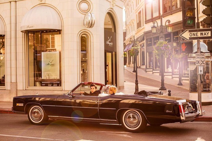 A black convertible car parked on a city street with a dog in the passenger seat. 1