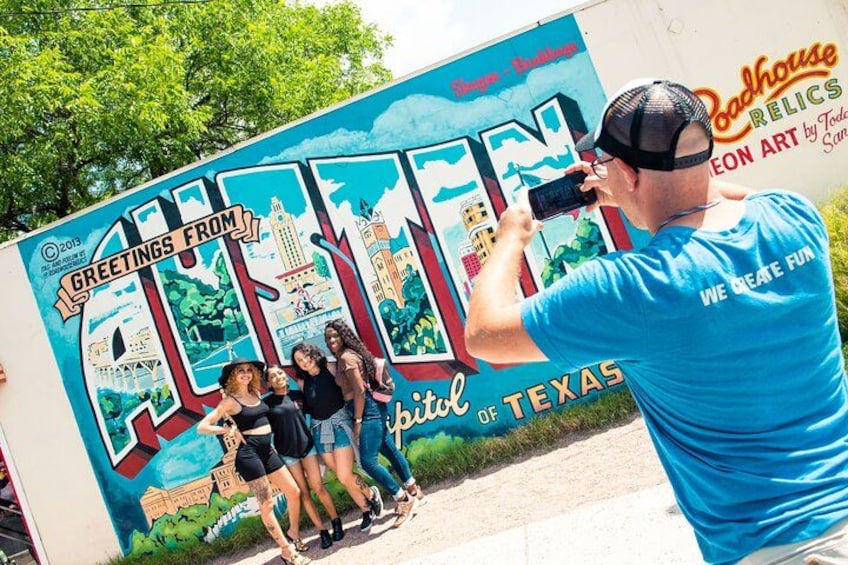 A mural with 'Greetings from Austin, Texas' and 'Coahues Relics' text, a person taking a photo, and a group of people posing in front of it. 1