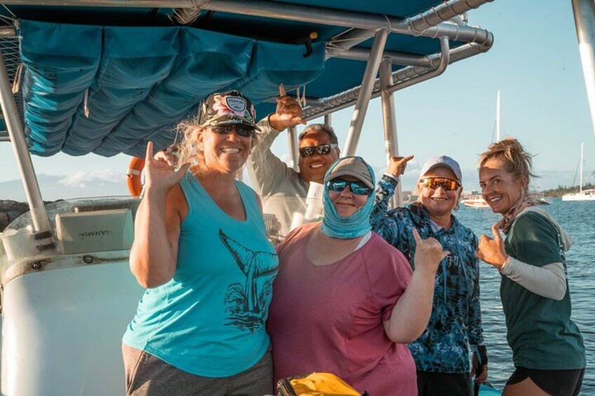 A group of people on a boat with a blue canopy, water, and sailboats in the background. 4