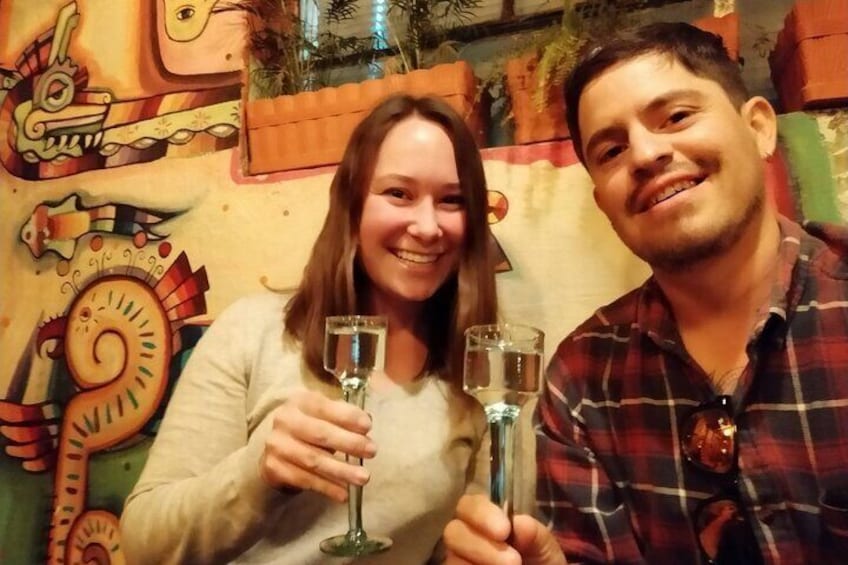 Two people holding glasses, with a colorful mural in the background. 1