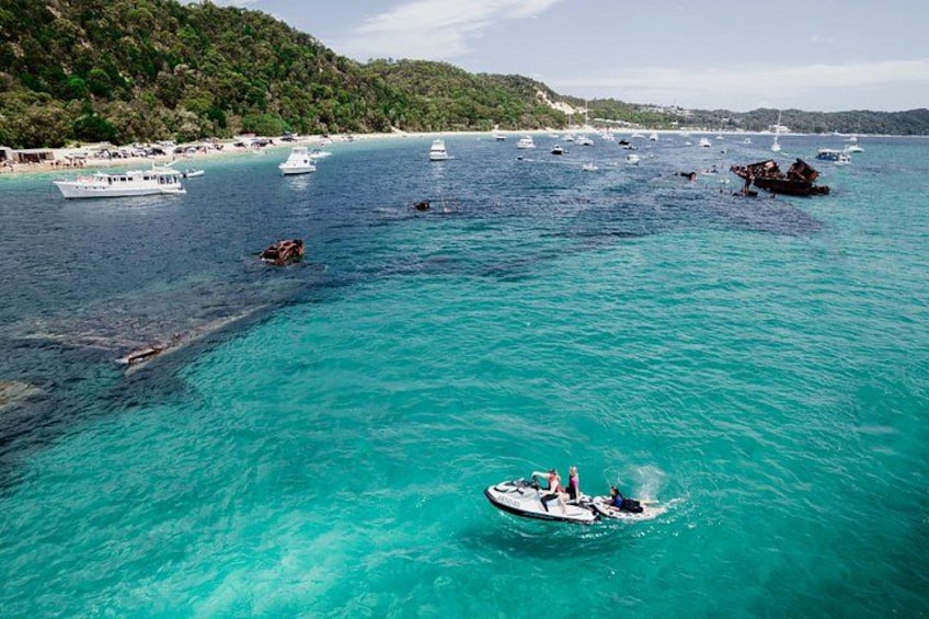 Un mar turquesa con barcos, una lancha con gente y una playa con sombrillas. 5