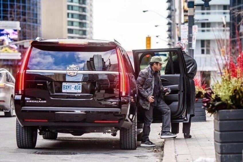 Un SUV negro con la puerta trasera abierta, un hombre de pie a su lado y una placa de matrícula que dice  2