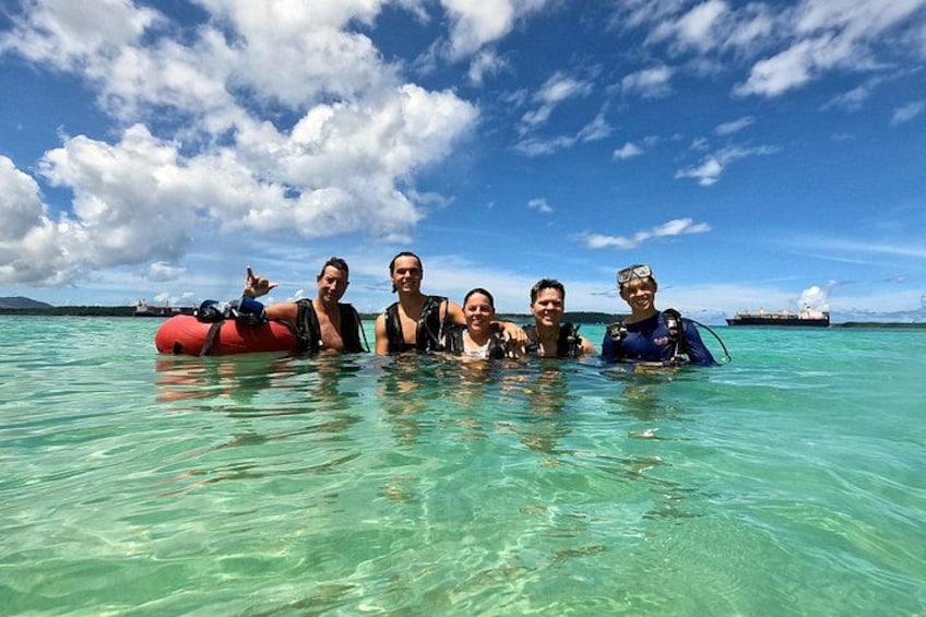Un grupo de personas en agua turquesa cristalina con un barco al fondo. 4