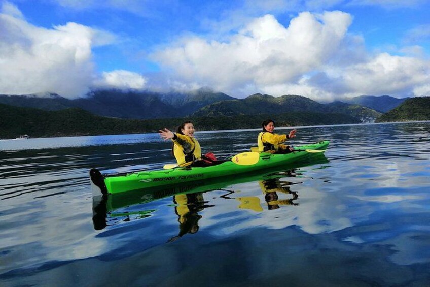 Two people kayaking on a calm lake with mountains in the background. 1