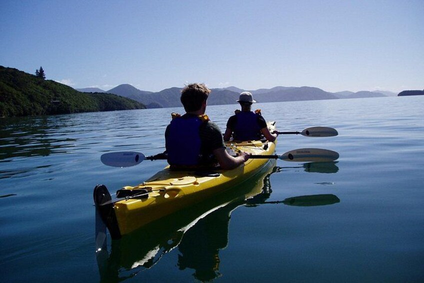 Two people kayaking on a calm lake with mountains in the background. 2
