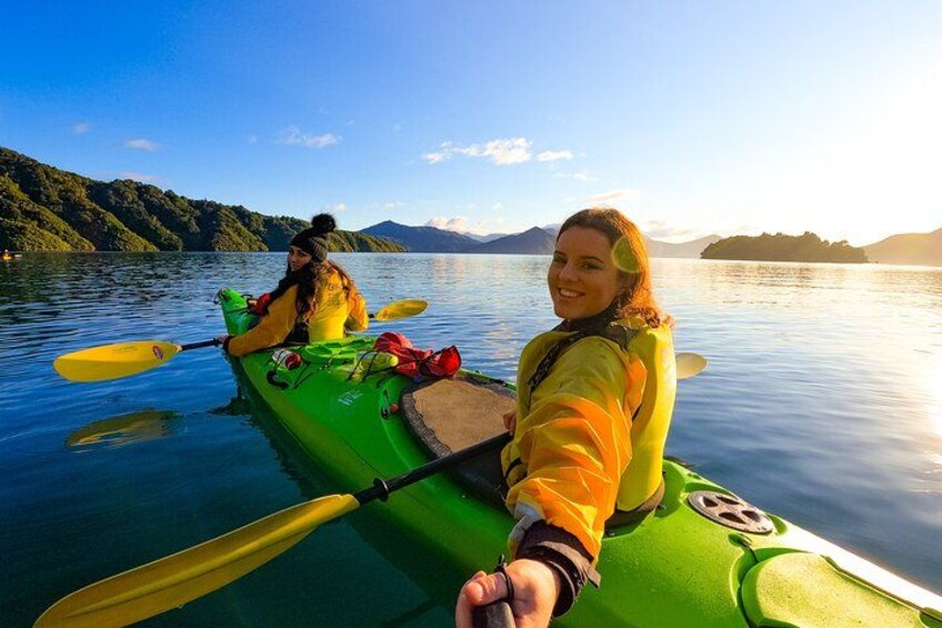 Two people kayaking on a calm lake with mountains in the background. 1