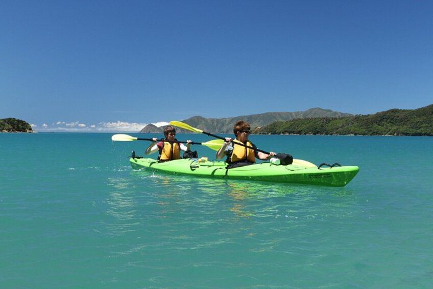 Two people kayaking on a calm turquoise sea with a clear sky and distant mountains. 4