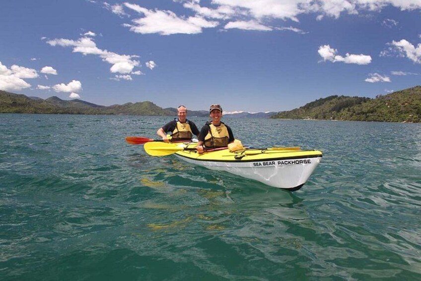 Two people in a kayak on a calm lake with mountains in the background. 3