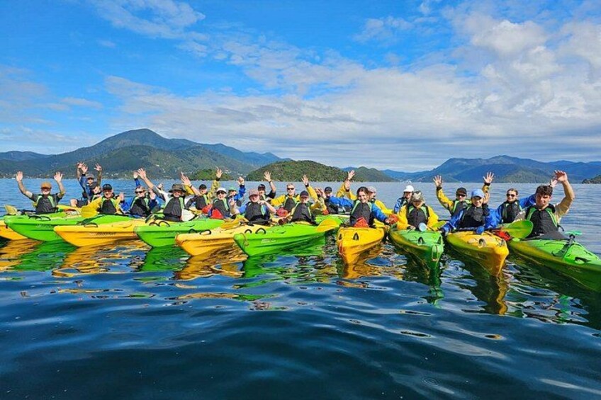 A group of people in green kayaks on a calm lake with mountains in the background. 5