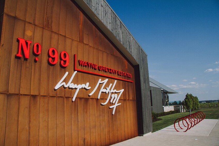 A building with a wooden facade, a large red sign reading 'No 99 Wayne Greyzy Estates,' and a smaller sign with a signature. 1