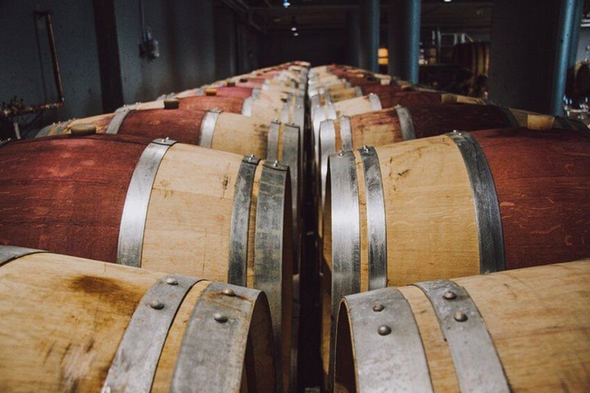 Rows of wooden barrels with metal bands, likely in a storage or aging facility. 5