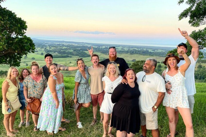 Un grupo de personas de pie en una colina cubierta de hierba, con una vista panorámica de un valle y una masa de agua a lo lejos. 2