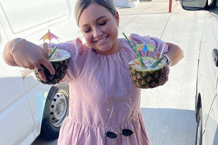 A person holding two coconuts with straws and a small umbrella. 5