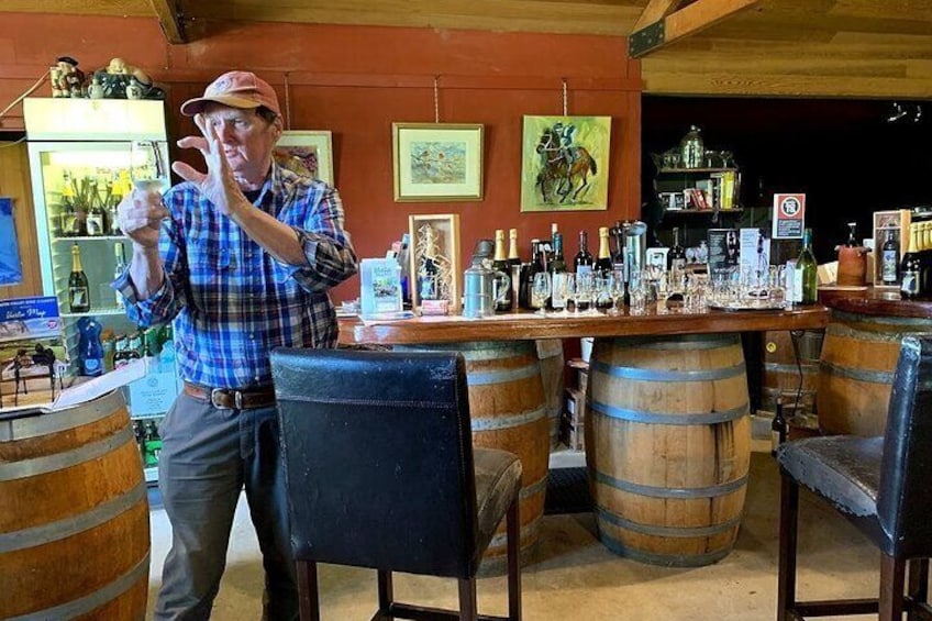 A man in a plaid shirt and cap standing at a bar with wooden barrels and chairs. 3