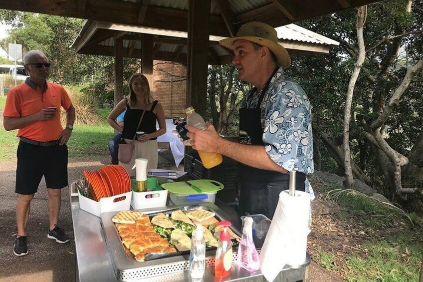 A food stall with sandwiches and drinks, a person serving food, and a covered area with trees in the background. 4