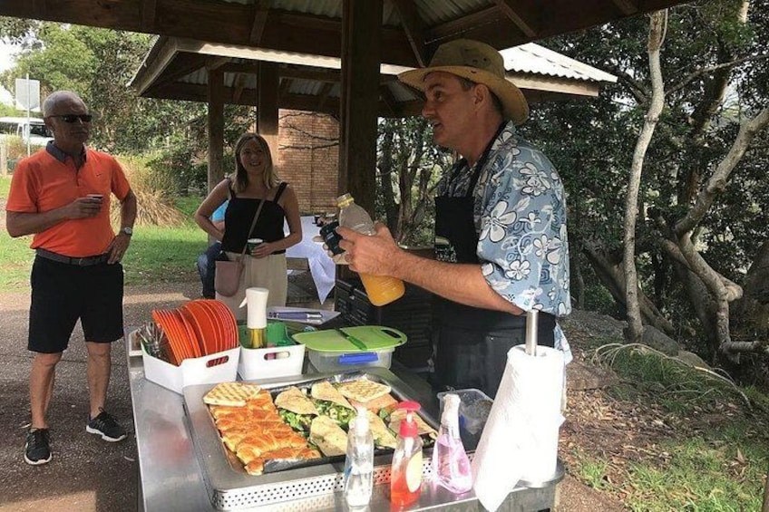 A food stall with sandwiches and drinks, a person serving food, and a covered area with trees in the background. 3