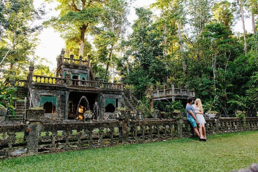A couple embracing in a lush garden with a stone bridge and a gazebo. 1