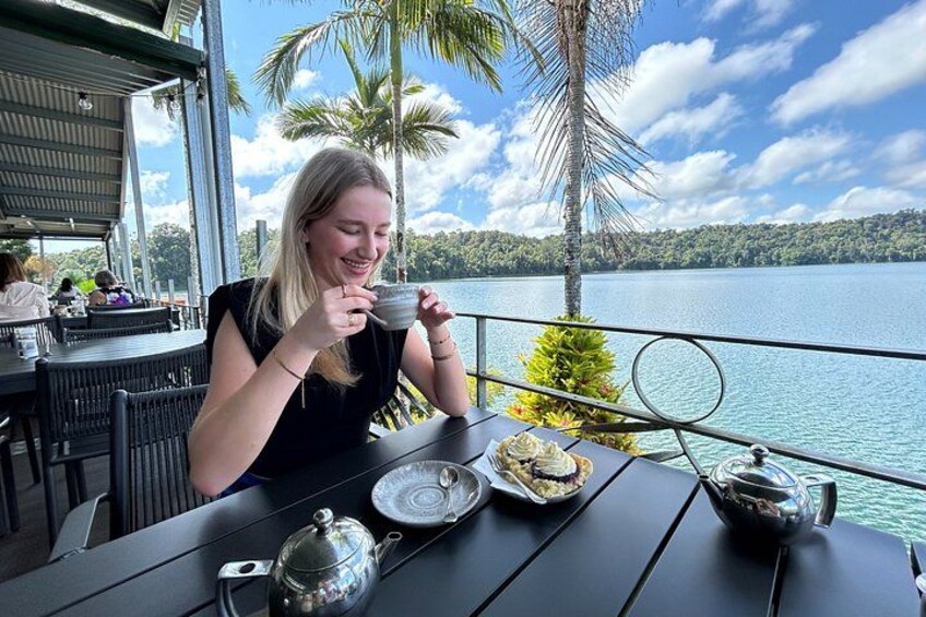 A person sitting at a table with a teapot and cups, overlooking a lake with palm trees and a clear sky. 2