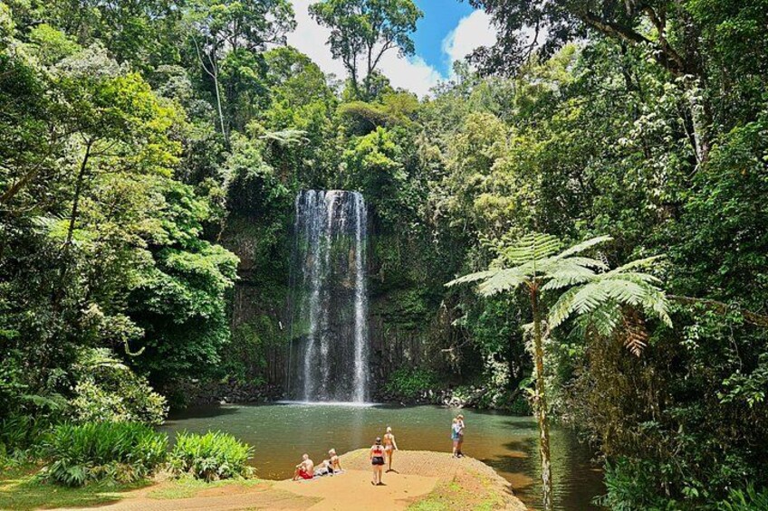 Una cascada en un área boscosa con un pequeño estanque y gente sentada junto al agua. 5