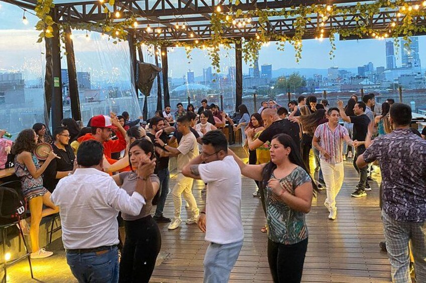 En grupp människor som dansar på ett trädäck med en stadsbild i bakgrunden. 1