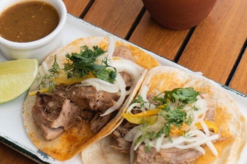 Två tacos med kött, lök och koriander, serverade på en vit tallrik med en liten skål sås och en limeklyfta vid sidan om. 3