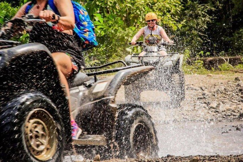 People riding ATVs on a muddy trail surrounded by greenery. 5