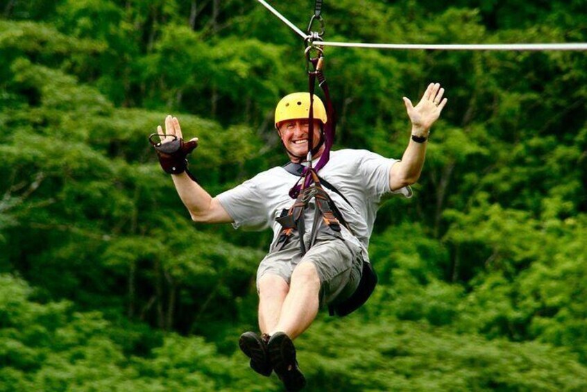 A person suspended in mid-air on a zip line, wearing a helmet and harness, with dense green foliage in the background. 4