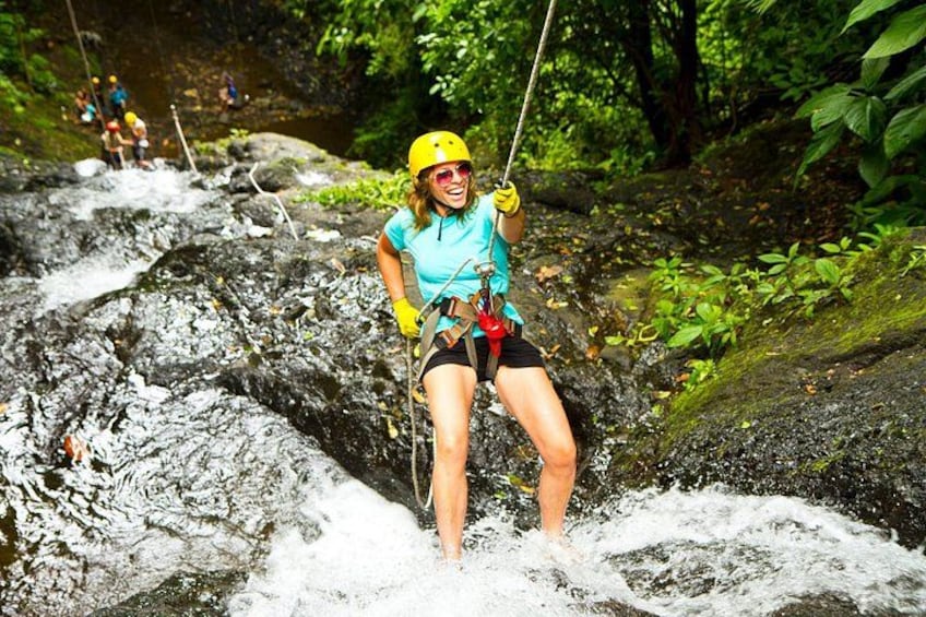 Una persona haciendo tirolesa sobre una cascada rocosa en una zona boscosa. 2