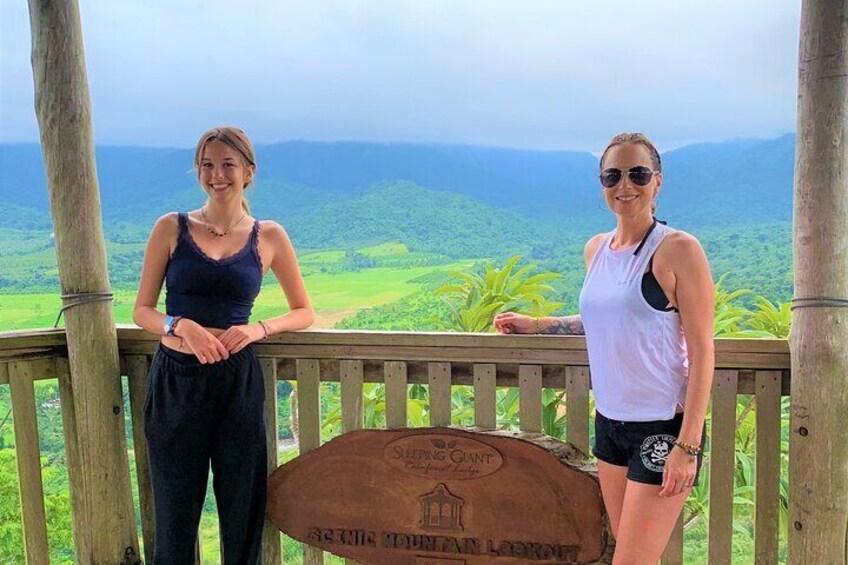 Two people standing on a wooden deck overlooking a lush landscape. 4