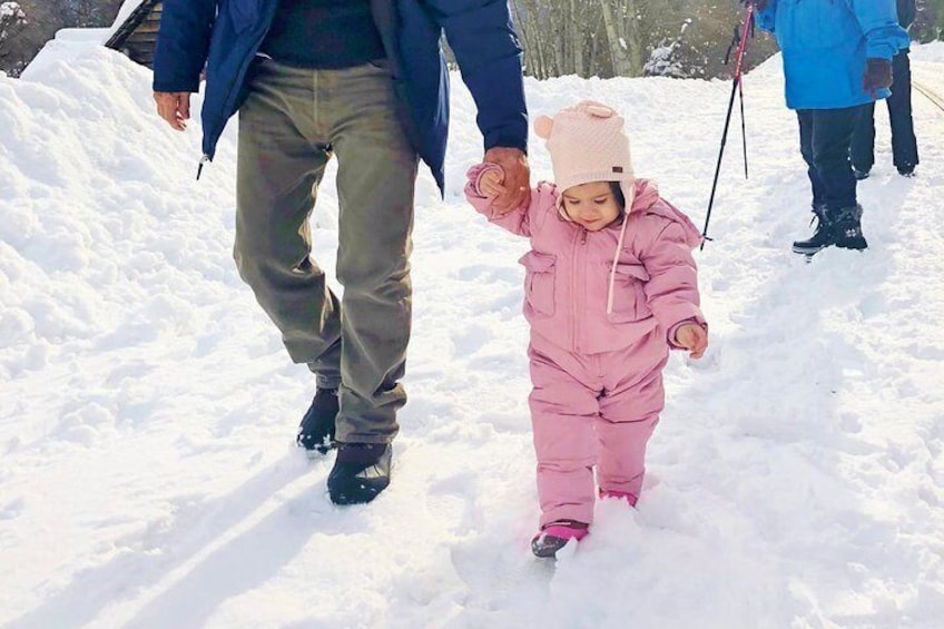 Un niño con traje rosa para nieve caminando sobre la nieve, agarrado de la mano de un adulto. 2