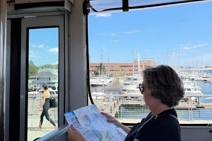 A person holding a map inside a boat, looking out at a marina with boats and a building in the background. 1