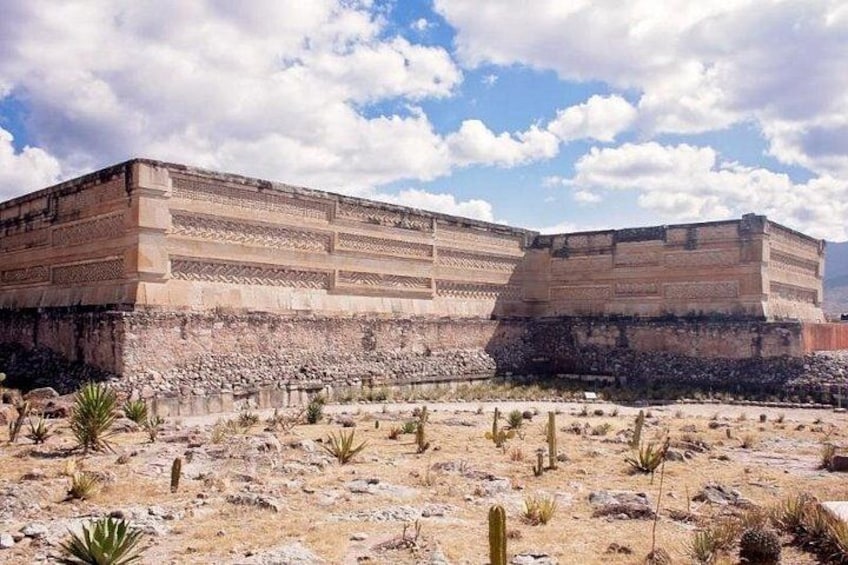 A large ancient structure with a flat top and stepped sides, surrounded by sparse desert vegetation. 4