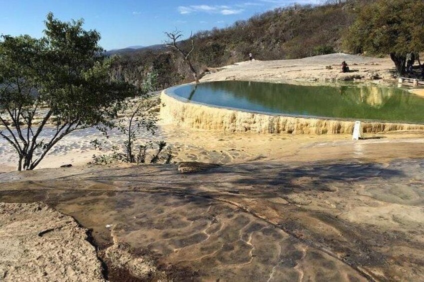A natural pool with a sandy shore, surrounded by sparse vegetation and a hilly landscape. 2