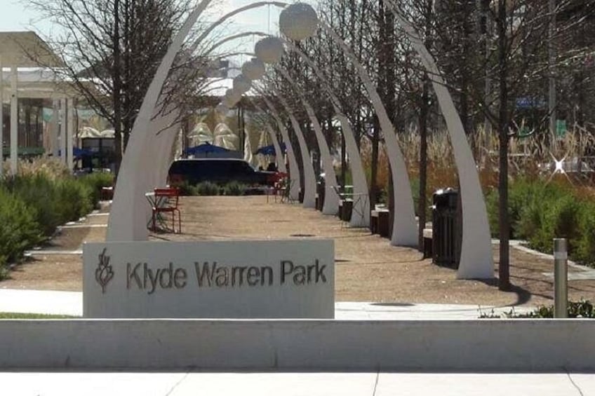 Een pad dat leidt naar een bord met de tekst 'Klyde Warren Park', met witte bogen erboven. 4